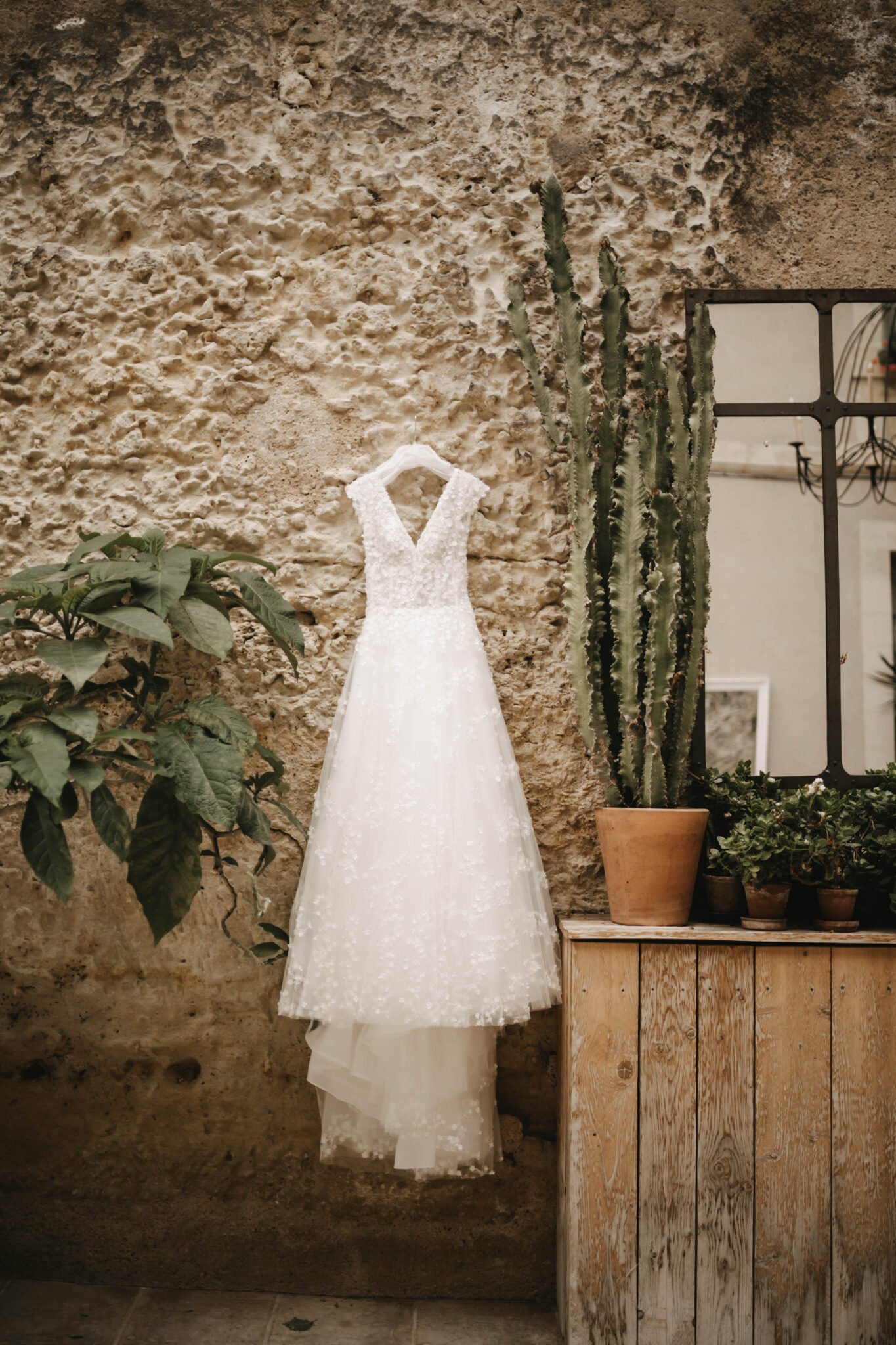 robe de mariée suspendue contre un mur en pierre avec des plantes